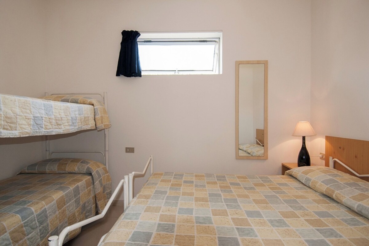 Een slaapkamer met twee bedden, een raam met gordijn, een nachtkastje met lamp en een spiegel aan de muur.