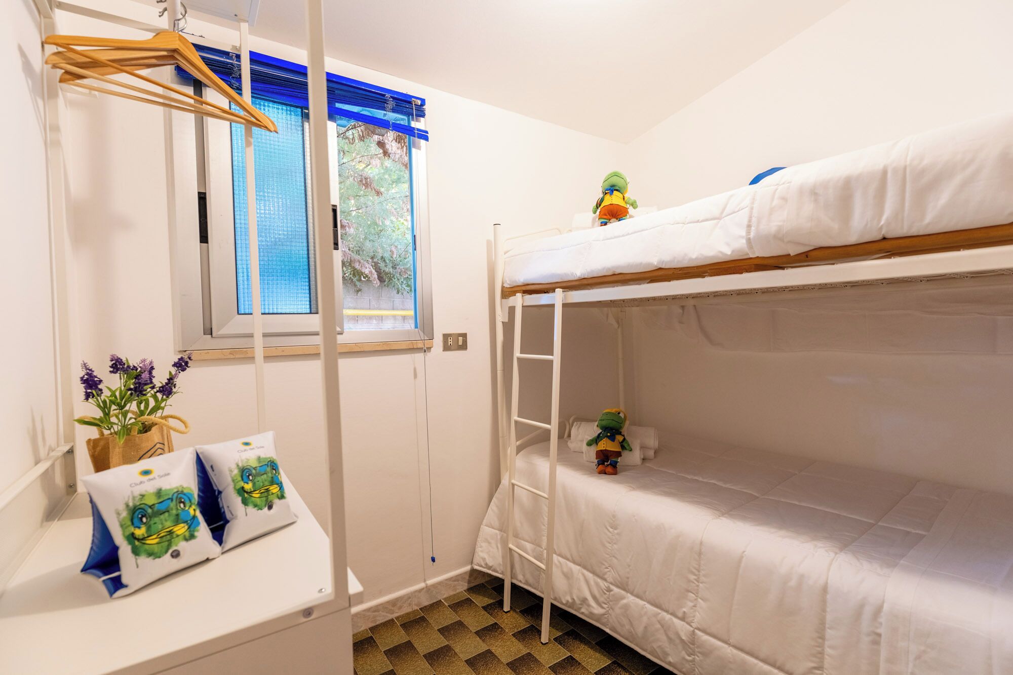 A bunk bed room with a window, a hanging plant, and a small shelf with items.