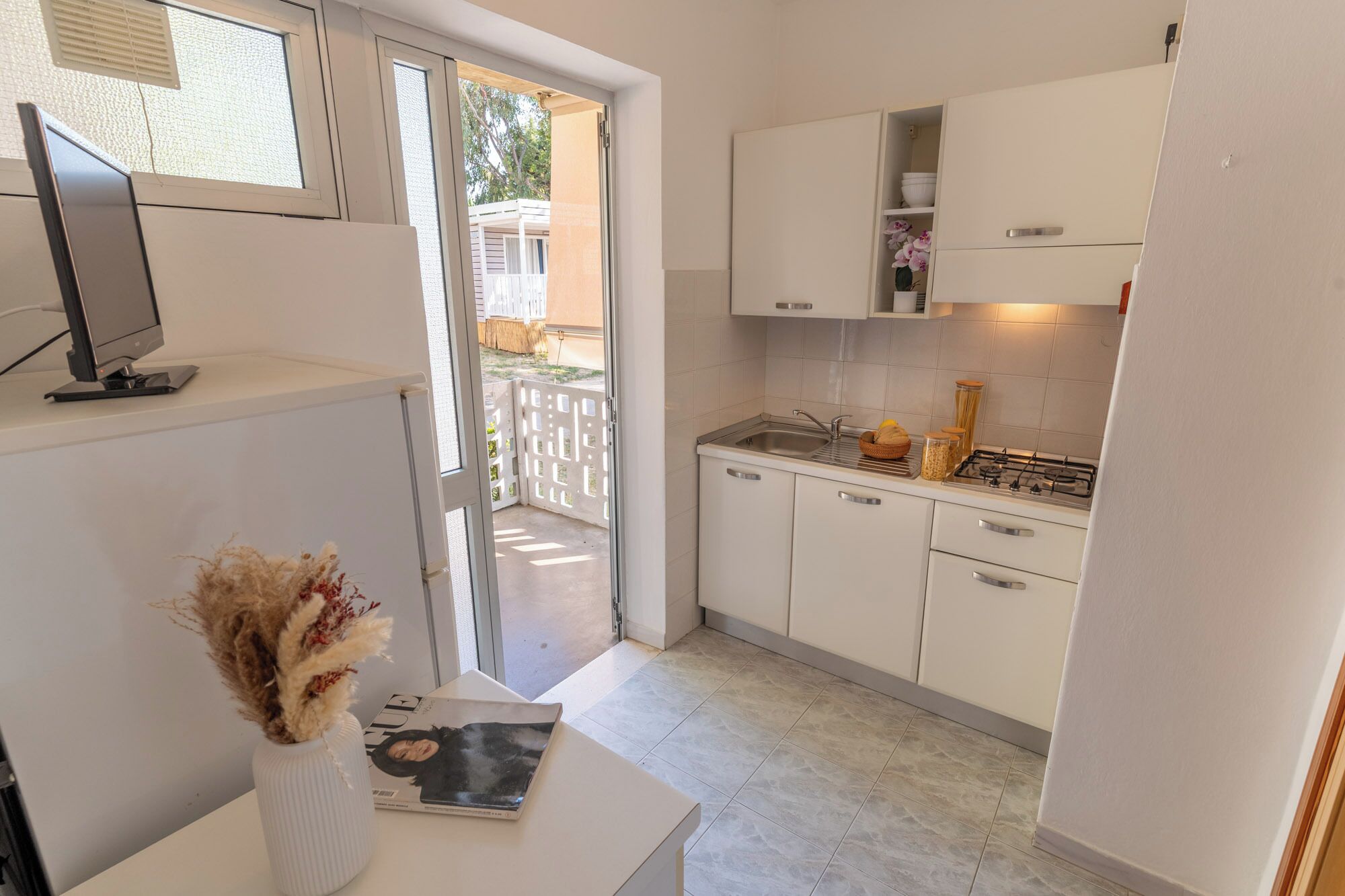 Une cuisine de taille réduite, avec des meubles blancs, une cuisinière à gaz et un petit évier.