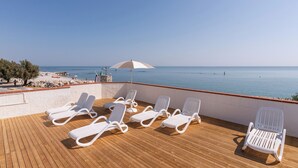 Een balkon met witte loungestoelen en een witte parasol met uitzicht op een strand.