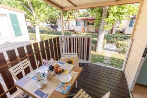 Un espace extérieur aménagé, abrité et doté de tables préparées pour le petit-déjeuner, entouré d’une terrasse en bois et d’une clôture blanche.