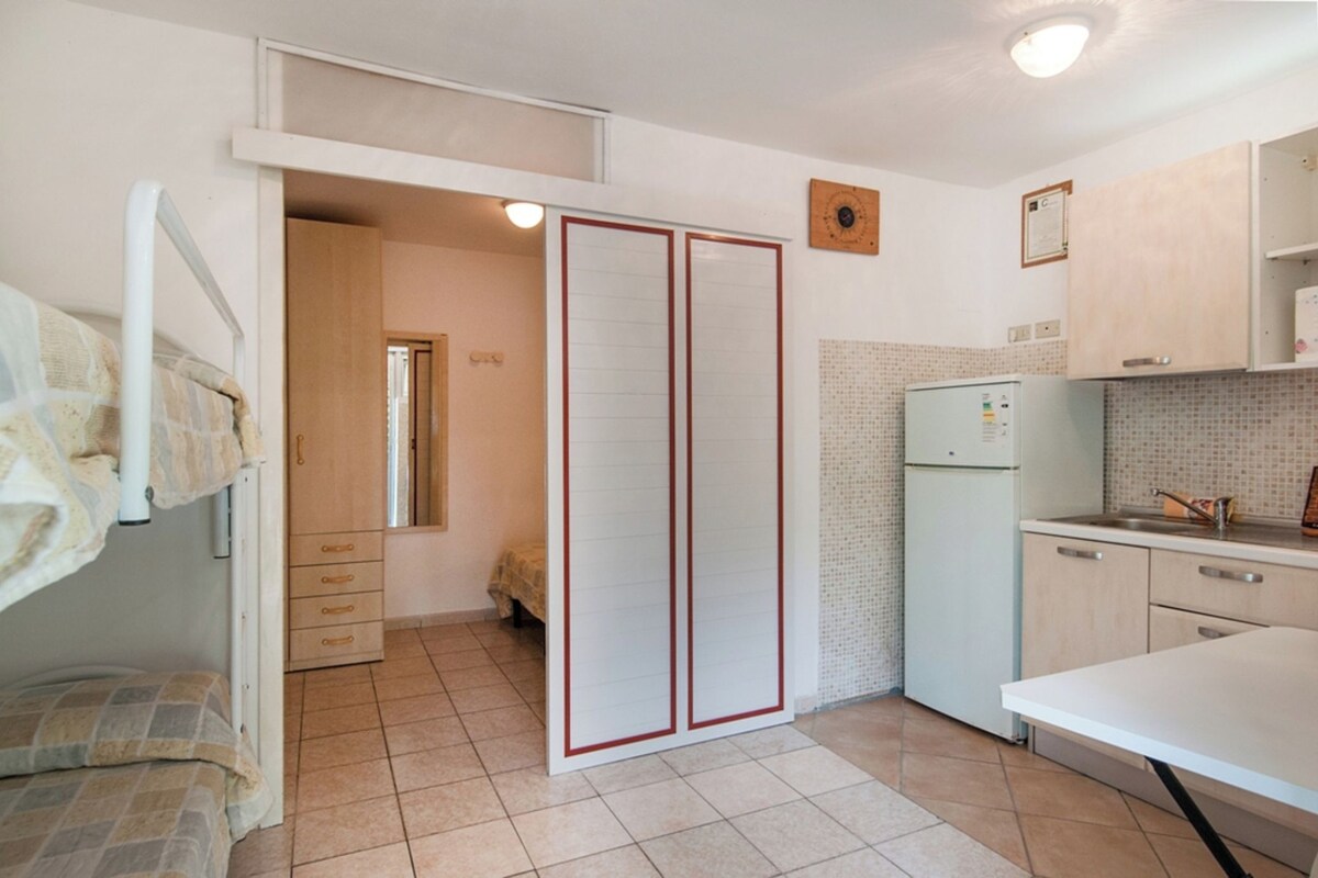 Ein kleines Zimmer mit Etagenbett, einer Küchenzeile und einem Schiebetürenschrank.