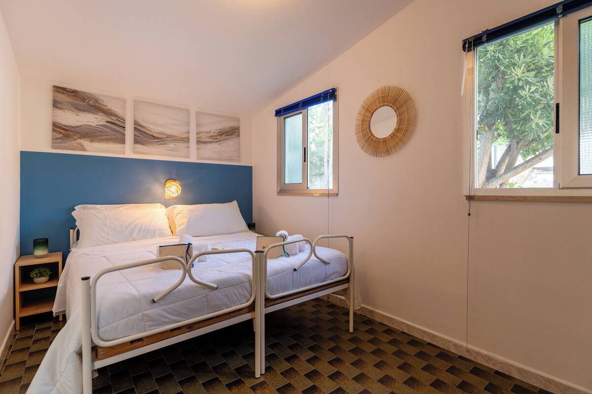 A bedroom with a bed, bedside table, wall art, a window, and a floor with a checkered pattern.