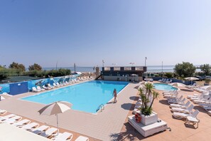 Une piscine avec des chaises longues et des parasols, une bouée de sauvetage, et une vue sur la mer.