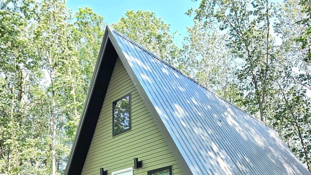 Eine kleine Holzhütte mit einem grünen Dach und einer weißen Tür, umgeben von einem angelegten Garten mit Steinen und Pflanzen.
