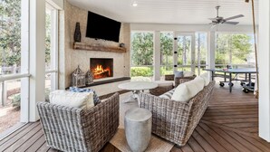 A covered outdoor area with a fireplace, wicker furniture, and a table. - Watercolor Home with LSV and Ping Pong (Santa Rosa Beach)