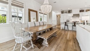 A spacious kitchen with a wooden dining table and chairs, a large chandelier, and white cabinetry. - Watercolor Home with LSV and Ping Pong (Santa Rosa Beach)