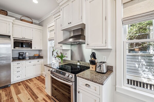 A modern kitchen with white cabinetry, a stainless steel range hood, a built-in microwave, and a granite countertop.