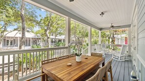 A covered outdoor dining area with a wooden table and wicker chairs, surrounded by a white railing.