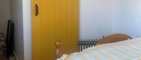 Una habitación con una puerta corredera amarilla, una cama con colcha estampada floral, un radiador y un cabecero de madera.