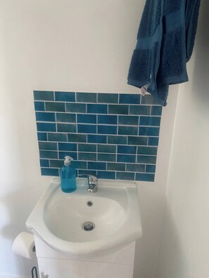 Ein Badezimmer mit weißem Waschbecken, blauem Seifenspender und einer blauen Fliesenwand.