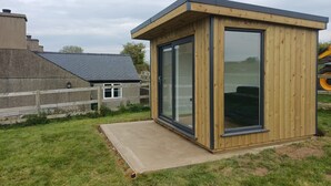 A small wooden structure with a glass door and a concrete platform. - Bryn-Mawr - two bedroom traditional farm holiday cottage with outstanding views (Caernarfon)