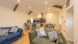 A living room with a blue sofa and a green sofa, both with cushions. There is a kitchen area in the background with a dining table and chairs. - Bryn-Mawr - two bedroom traditional farm holiday cottage with outstanding views (Caernarfon)
