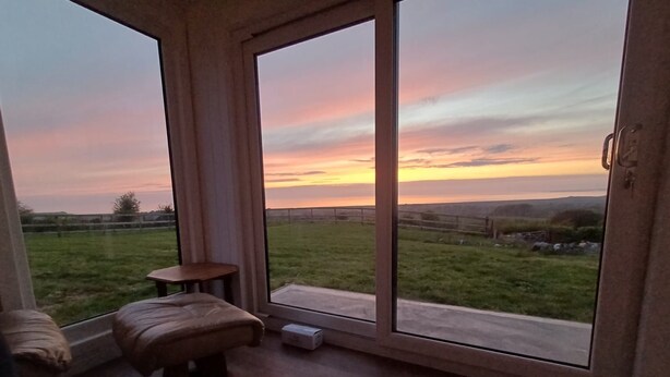 A room with a view of a sunset, a sliding glass door, a small table, and a cushioned bench. - Bryn-Mawr - two bedroom traditional farm holiday cottage with outstanding views (Caernarfon)