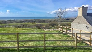 A coastal view with a stone building, a wooden fence, and a clear sky. - Bryn-Mawr - two bedroom traditional farm holiday cottage with outstanding views (Caernarfon)