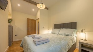 A bedroom with a bed, bedside lamps, a wooden wardrobe, and a ceiling light fixture. - Bryn-Mawr - two bedroom traditional farm holiday cottage with outstanding views (Caernarfon)
