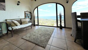 Amplia sala de estar con un gran ventanal con vista al mar, un sofá acogedor, una mesita y una estantería.