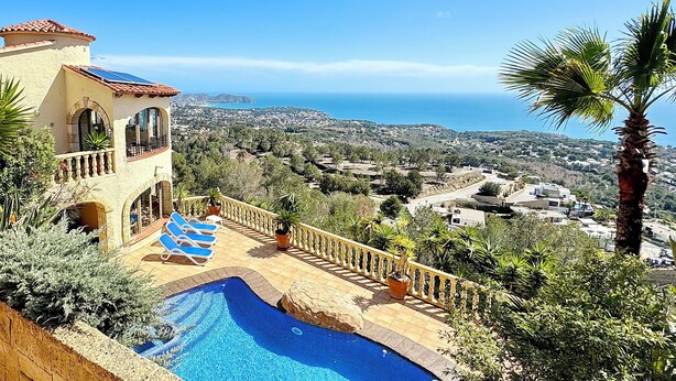 Zona de piscina con vistas al mar, un edificio con balcón y vegetación circundante.
