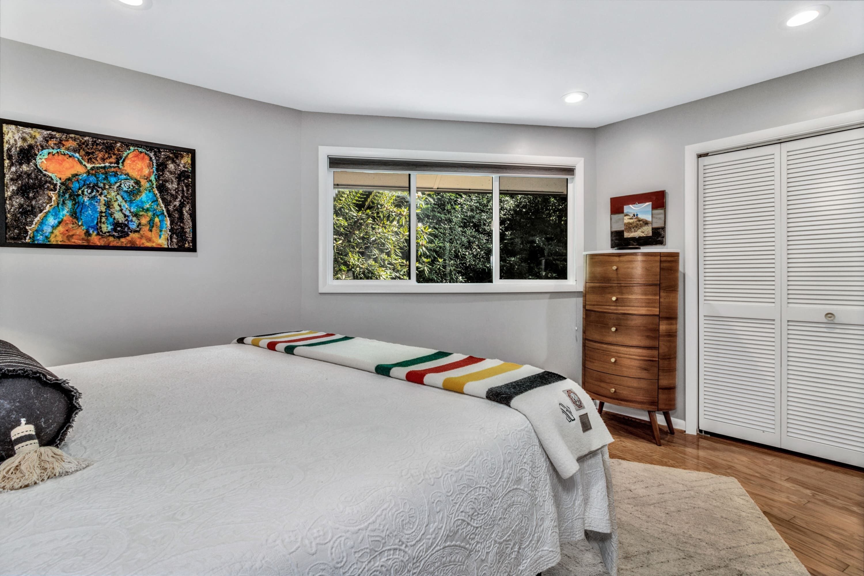 Un dormitorio con cama, ventana, armario y un cuadro en la pared.