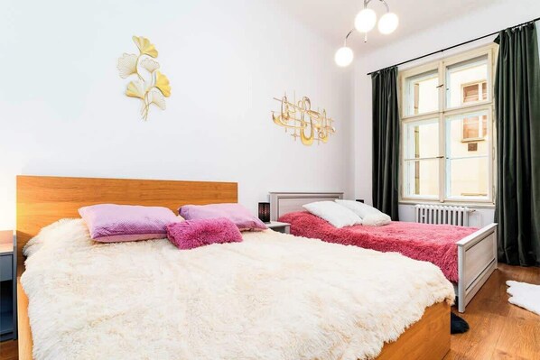 A bedroom with a large bed, two bedside tables, a wooden headboard, and a window with curtains.