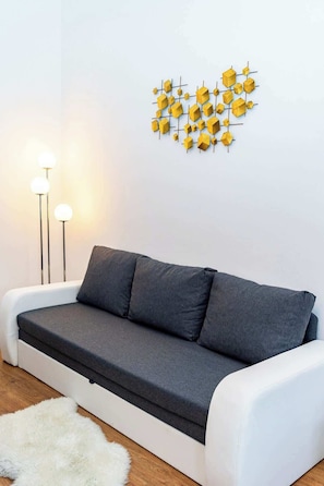 Uma sala de estar moderna com um sofá cinzento, um tapete branco e uma obra de arte geométrica amarela na parede.