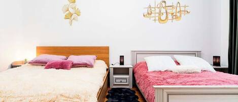 Een slaapkamer met twee bedden, elk met een deken in een andere kleur, een nachtkastje met een lamp en decoratieve wandkunst.