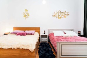 A bedroom with two beds, each with a distinct color blanket, a nightstand with a lamp, and decorative wall art.