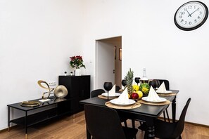 A dining area with a black table set for two, a clock on the wall, and a plant on a side table.