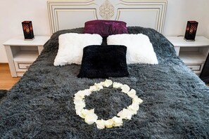 A bed with a fluffy grey blanket, white and black pillows, and a white flower arrangement.