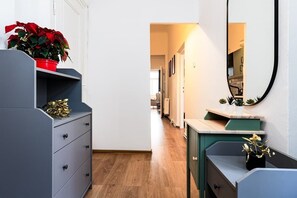 A hallway with a grey dresser, a red potted plant, a mirror, and a wooden floor.