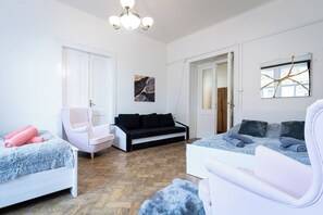 A modern living room with a white sofa, a black sofa, and a white armchair. There is a wooden floor and a chandelier. - Victory King's Residence (Prague)