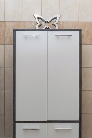 A white wardrobe with two doors and a handle, set against a tiled wall.