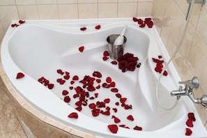 A bathtub with red rose petals and a champagne bottle.
