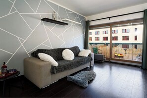 A modern living room with a sofa, a small table with a bottle and glasses, and a view through a large window to an outdoor area. - Penthouse Tiger (Prague)