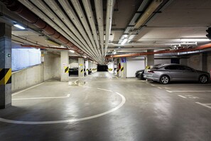 A multi-level parking garage with concrete pillars, directional arrows, and a car parked on the right. - Penthouse Tiger (Prague)