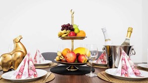 A three-tiered fruit stand with a golden hook, surrounded by plates with floral napkins, a golden heart-shaped object, and a champagne bucket. - Grand Luxury Suite Su (Prague)