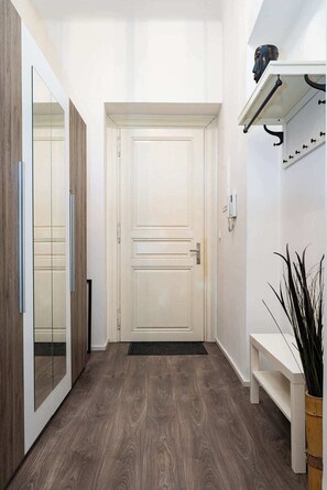 A hallway with a wooden floor, a white door, a bench, and a plant.