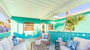 Ein überdachter Patio-Bereich mit Korbmöbeln, einem Holztisch und einer türkisblauen Wand.