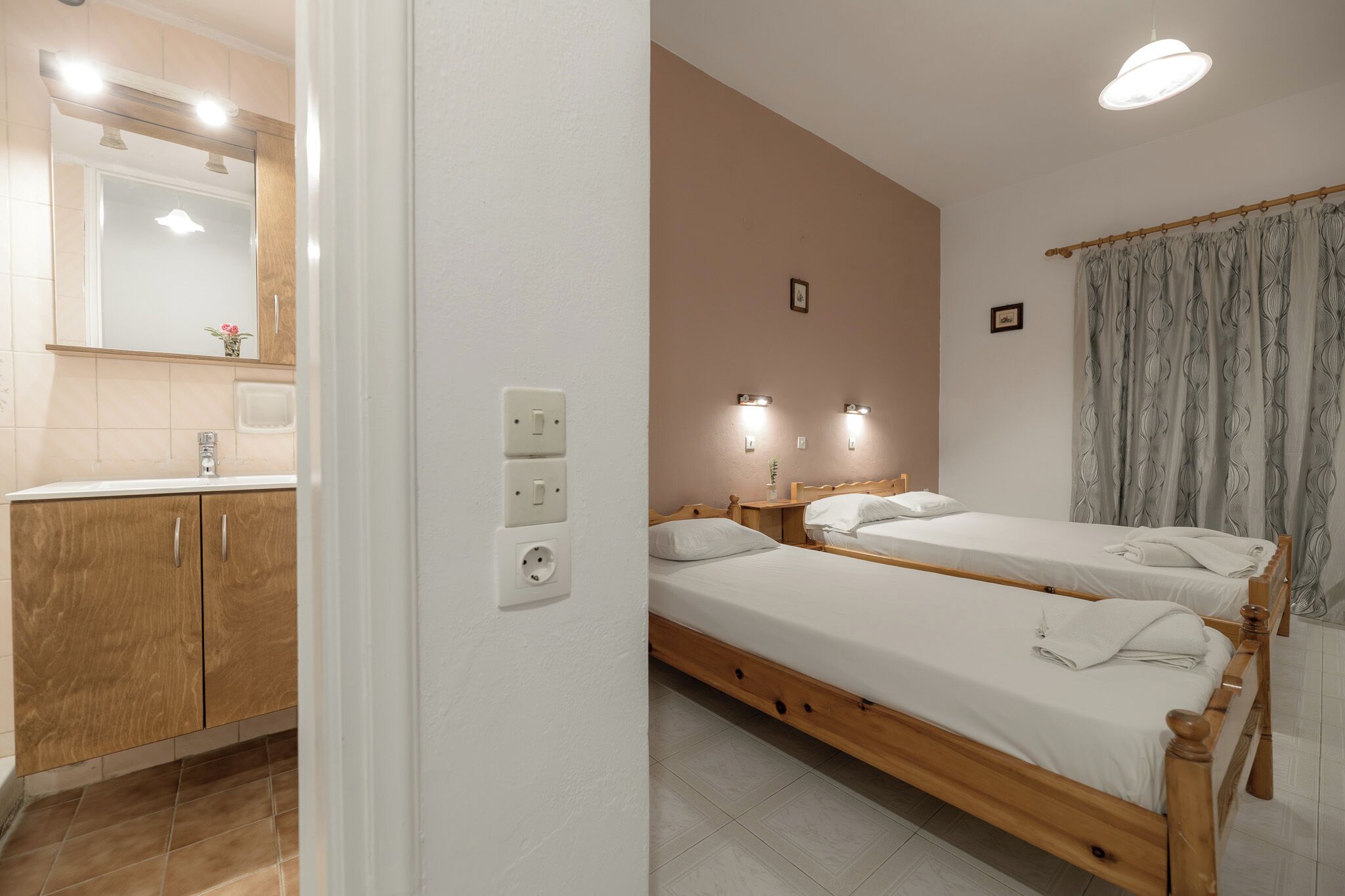 A bedroom with two single beds, a wooden wardrobe, a bathroom with a mirror, and a shower.