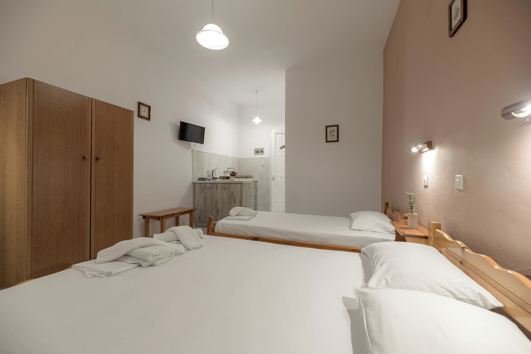 Une chambre d’hôtel avec deux lits simples, une armoire en bois, une petite table, un téléviseur fixé au mur et une salle de bain visible à travers une porte ouverte.
