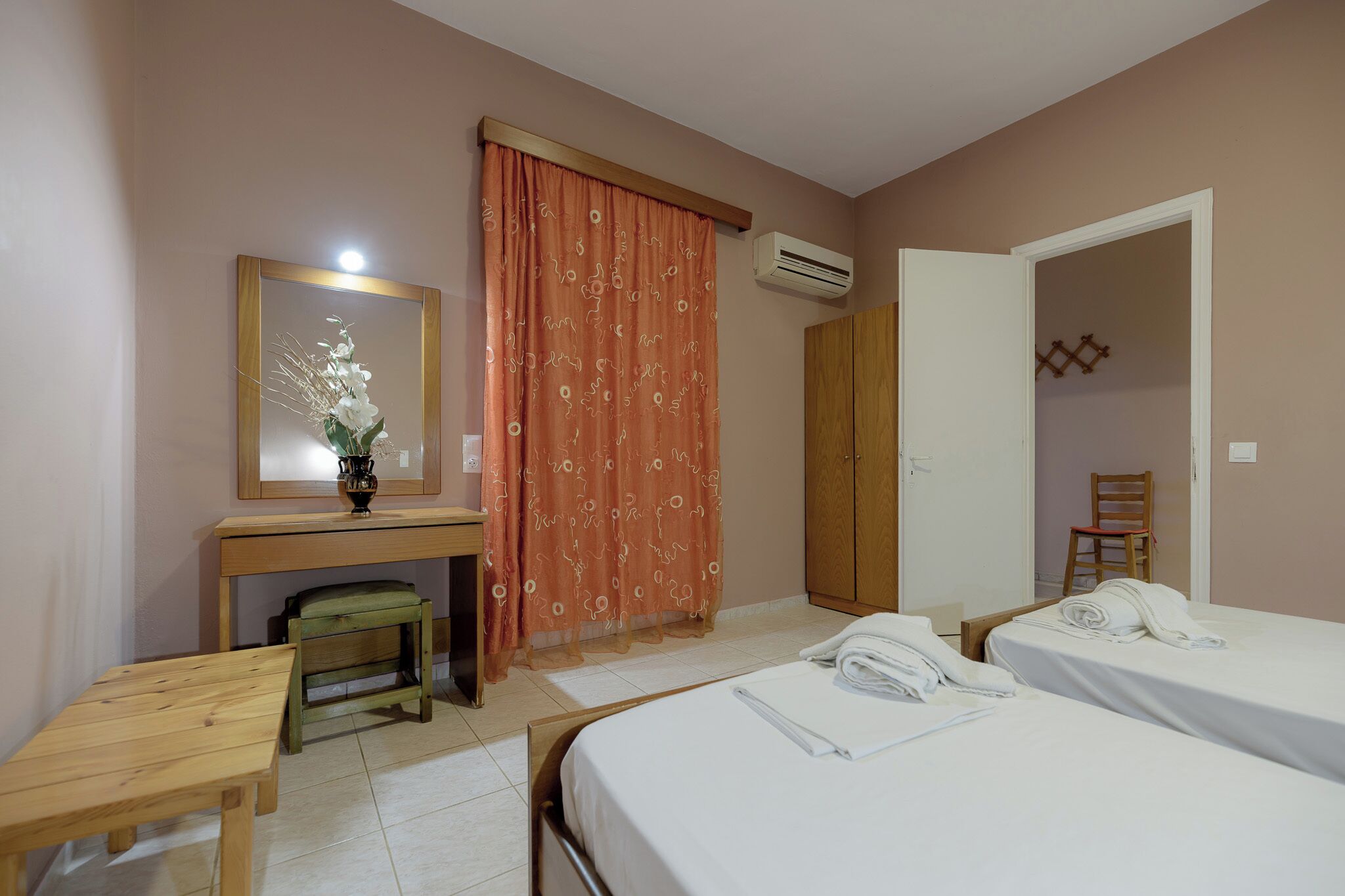 A hotel room with two beds, a desk with a mirror, a chair, and a wardrobe.