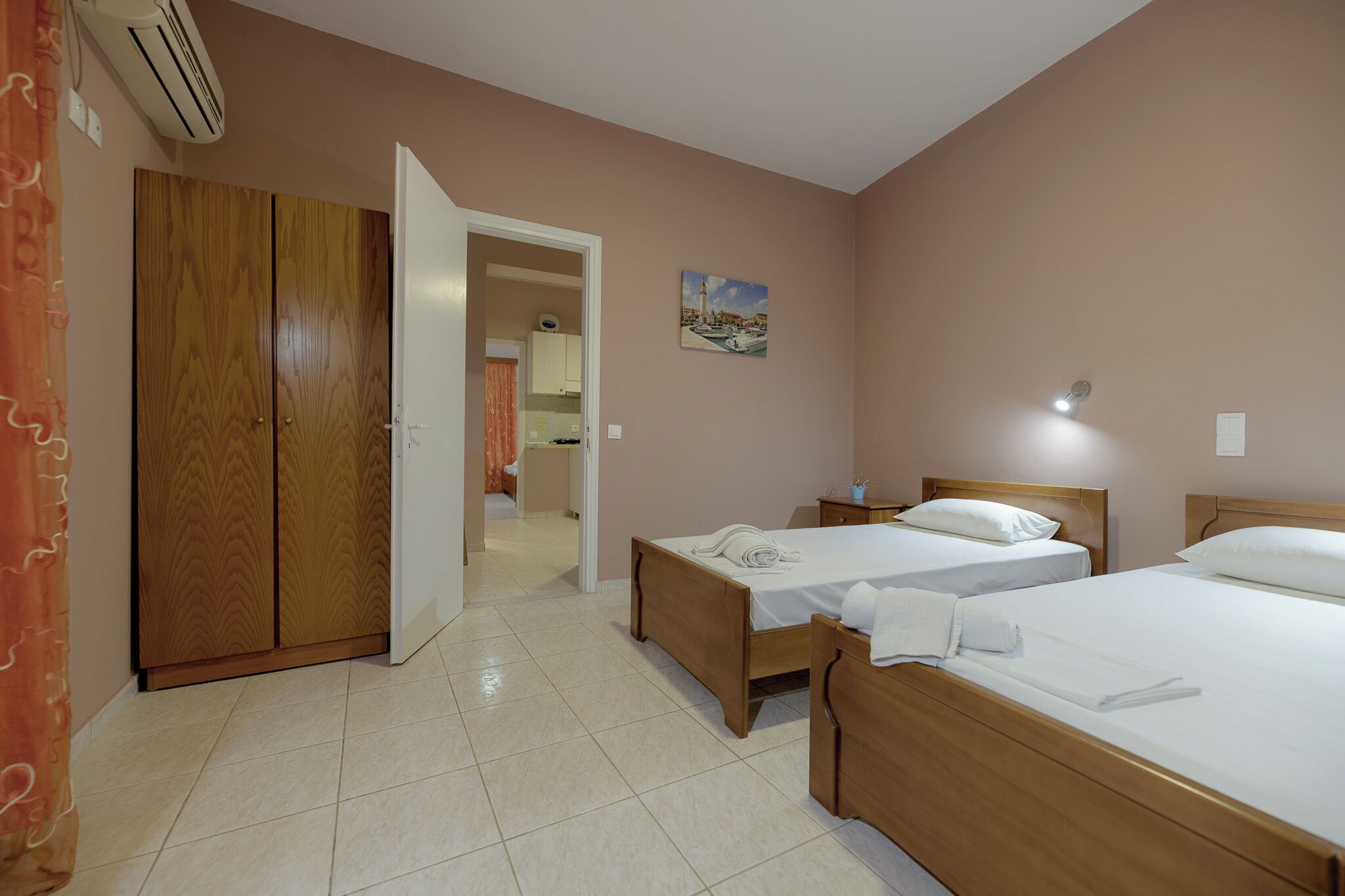 Ein Hotelzimmer mit zwei hölzernen Betten, einem Holzschrank, einem Bild an der Wand und einer offenen Tür zu einem Badezimmer.