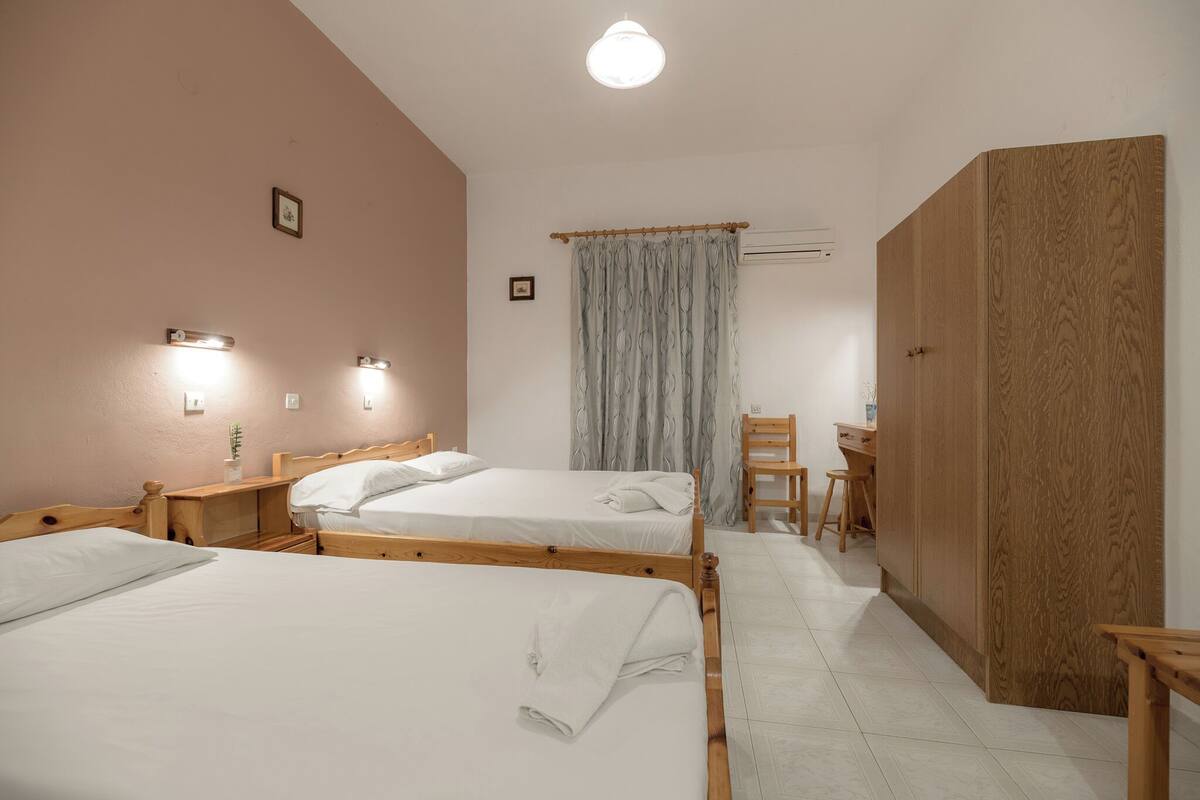 A hotel room with two beds, a desk, a wardrobe, and a shower area.