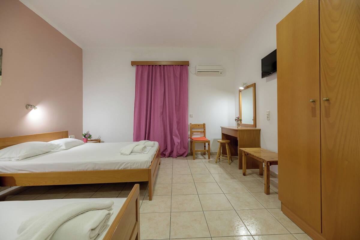 A bedroom with two wooden beds, a desk with a chair, a wardrobe, and a window with pink curtains.