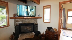 Ein Wohnzimmer mit Kamin, einem Fernseher auf einem Holzregal, einer Steinwand und Holzboden.