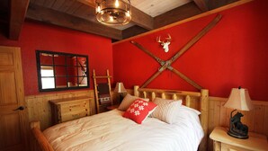 Ein Bett mit Holzbettrahmen, weiße Bettwäsche, eine rote Wand, ein Nachttisch mit einer Lampe und ein weiterer Holznachttisch.