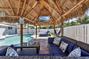 Un espacio al aire libre techado con piscina, asientos de descanso y una pantalla de televisión.
