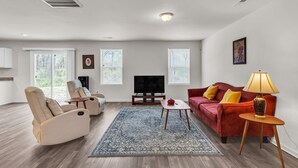A living room with a beige recliner, a red sofa, a coffee table, and a TV. - Quiet Retreat Perfect for Families 5 Bedroom Home (Rocky Mount)