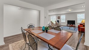 A spacious living room with a large wooden dining table, comfortable seating, a TV, and a view of the outdoors. - Quiet Retreat Perfect for Families 5 Bedroom Home (Rocky Mount)