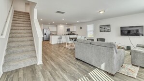 A modern apartment with a staircase, a living room with a grey sofa, a kitchen area, and a dining space. - 5br Retreat With Garage Parking 5 Bedroom Home (Rocky Mount)